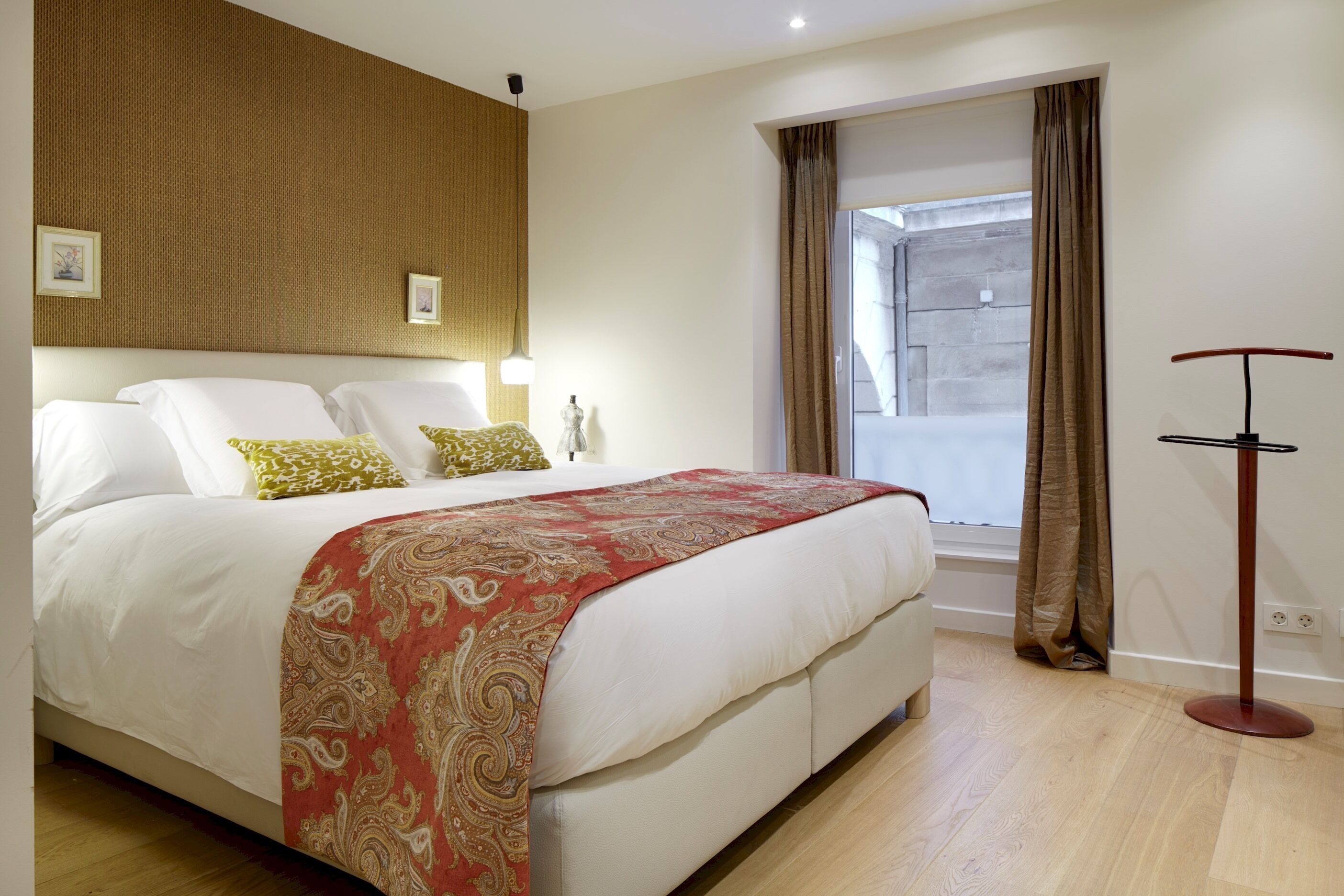 A hotel room with a large bed, a window with curtains, a standing lamp, and a wall-mounted light fixture.