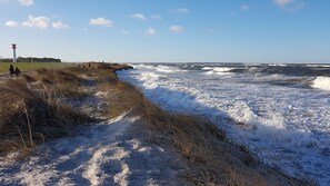 A beach with waves crashing onto the shore, a lighthouse in the background, and a grassy path leading to the water. - child and dog friendly holiday home complex (Wisch)