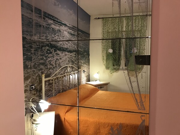 A bedroom with a bed, a nightstand, a lamp, a mirror, and a window with curtains.