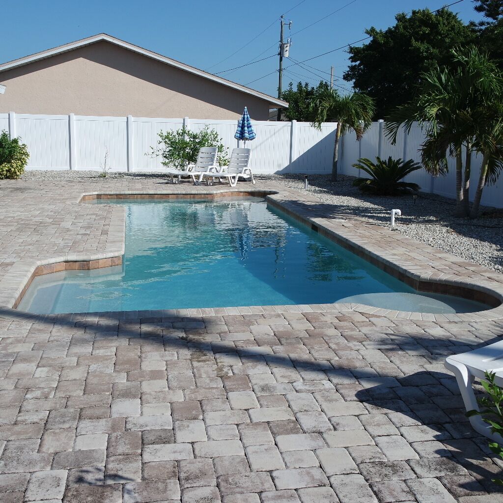 A swimming pool with a brick patio, white lounge chairs, and a palm tree in the background.
