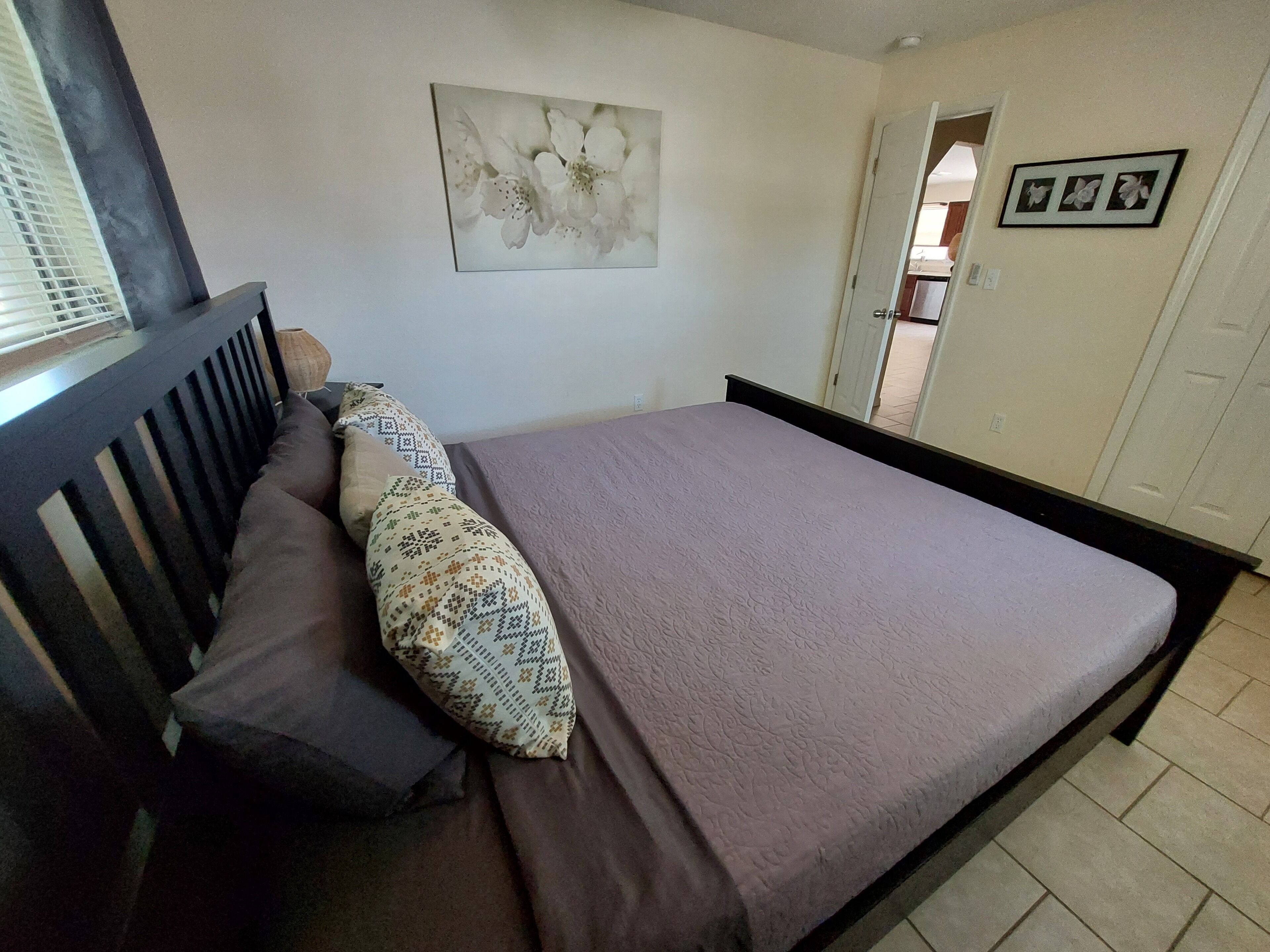 Un dormitorio con una cama, almohadas, una obra de arte colgada en la pared y una puerta que da a otra habitación.