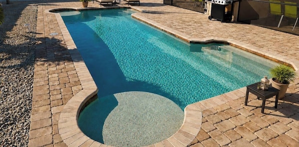 Una piscina con lettini, un barbecue e una veranda coperta.