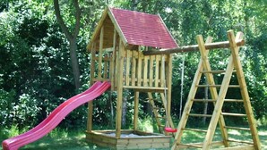 A wooden play structure with a red roof and a slide. - child and dog friendly holiday home complex (Heidkate)