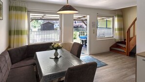 A cozy room with a dining table, chairs, a sofa, and a staircase leading to an upper level. - child and dog friendly holiday home complex (Heidkate)