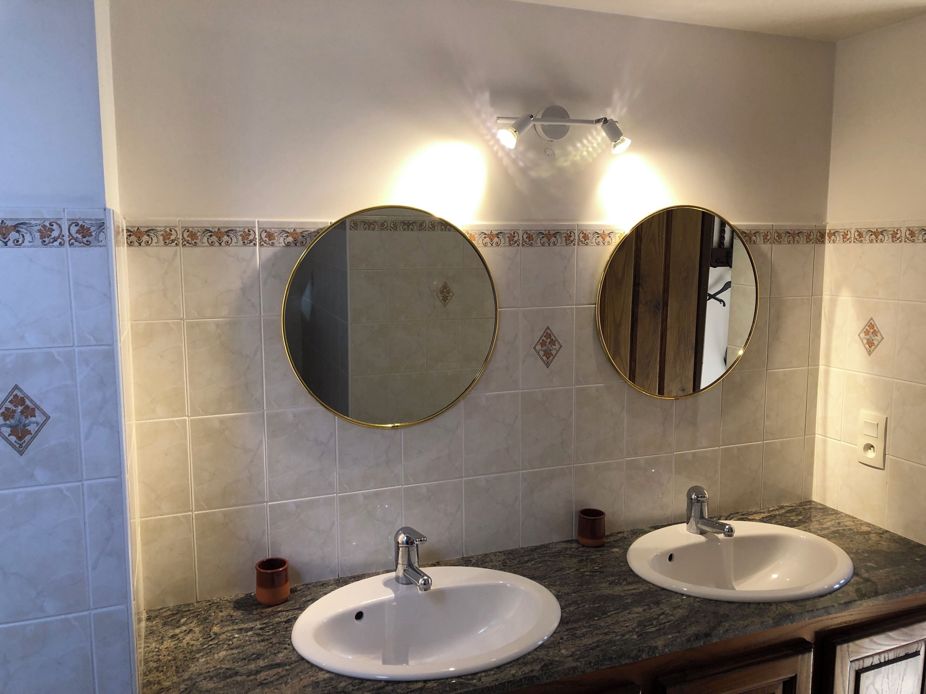 A bathroom with two sinks, a mirror, and a light fixture above the mirrors.