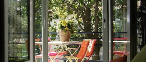 A balcony with a table and chairs, a wicker basket with flowers, and a view of trees and buildings.