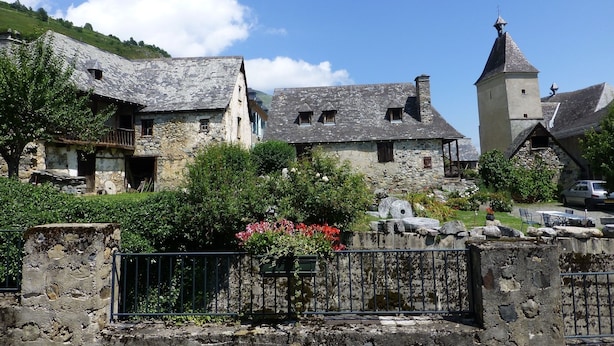 Un bâtiment en pierre doté d’une tour, entouré de verdure et surplombé d’un ciel dégagé.