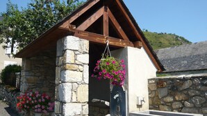 Un bâtiment en pierre avec un toit à pignon en bois, un escalier en pierre et des jardinières suspendues.