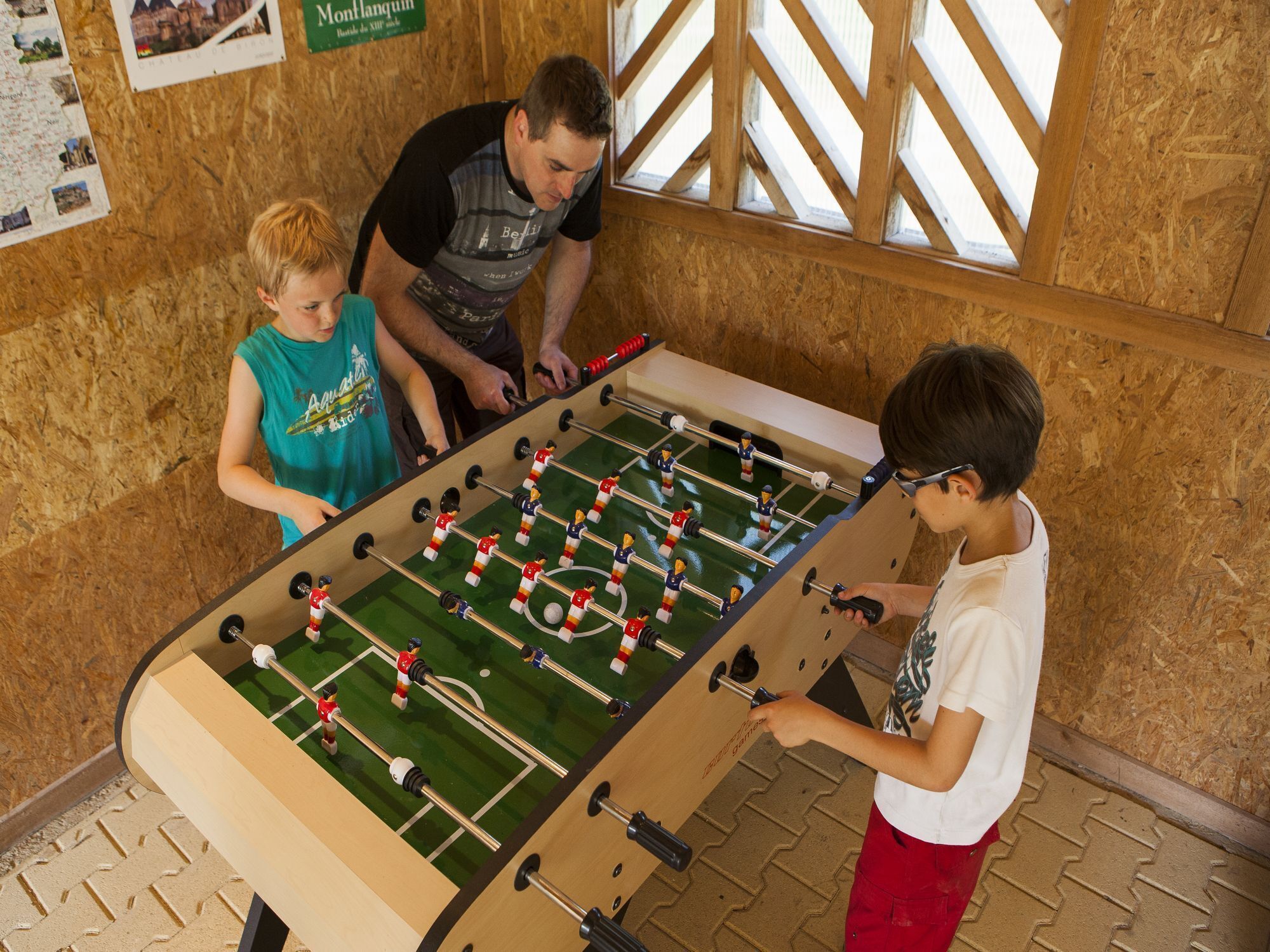 A foosball table in a room with wooden walls and a window with a lattice design.