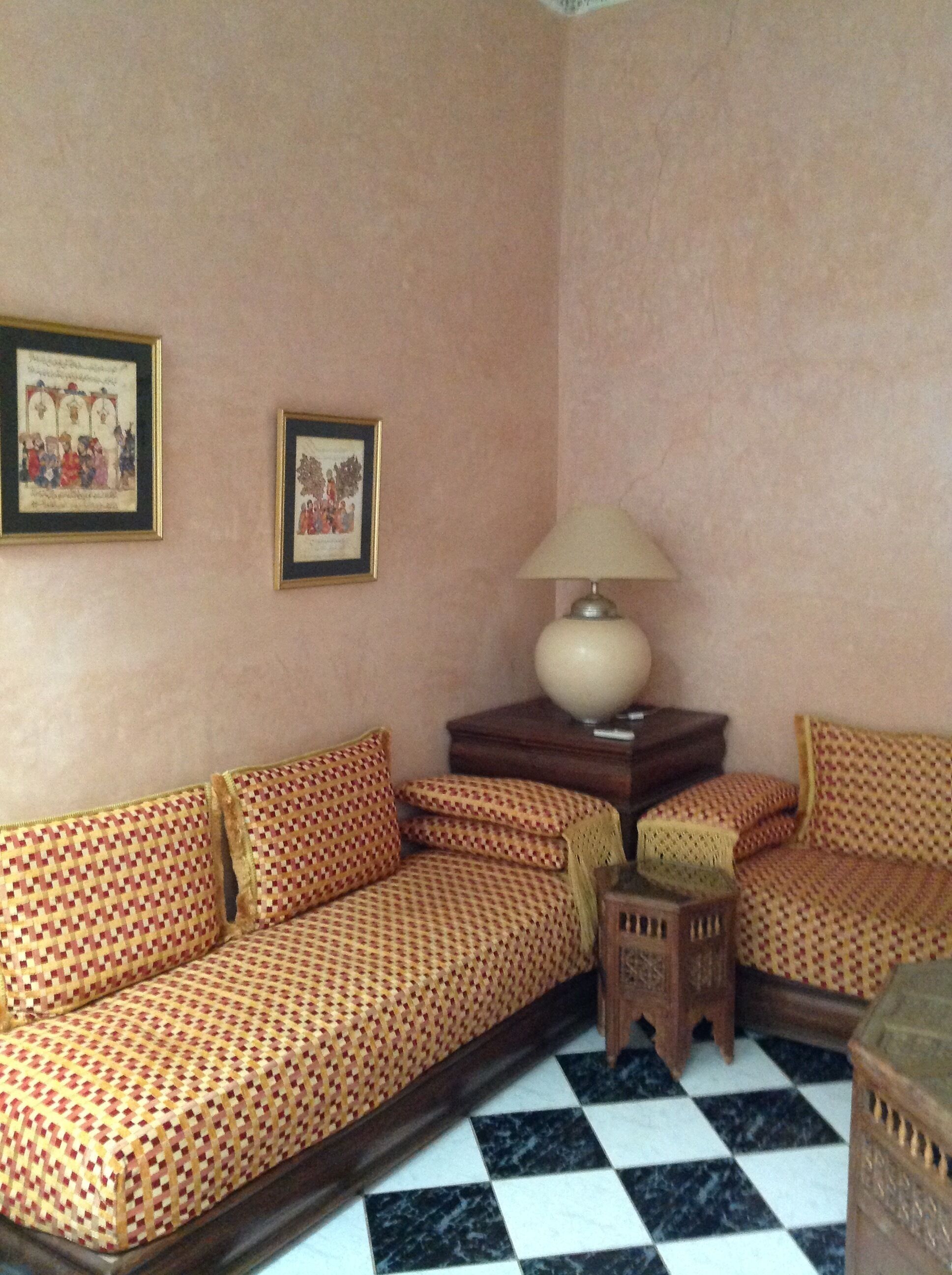 Una habitación con suelo de cuadros, sofá estampado, una mesita de madera con una lámpara y dos cuadros en la pared.