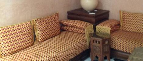Una habitación con suelo de cuadros, sofá estampado, una mesita de madera con una lámpara y dos cuadros en la pared.