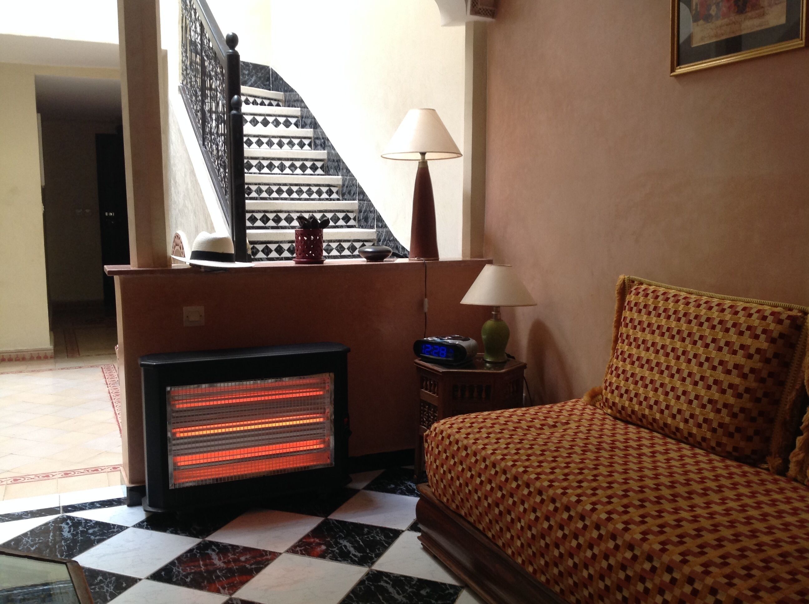 A hotel room with a bed, a heater, a lamp, a clock, and a staircase in the background.
