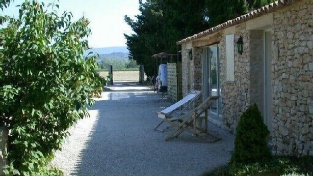 A stone building with a gravel driveway, a wooden bench, and a small tree. - Small Provence farm with pool, elegant accommodations (Joucas)