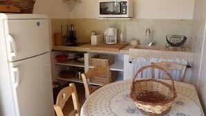 A compact kitchen with a refrigerator, microwave, and wooden shelves. - Small Provence farm with pool, elegant accommodations (Joucas)