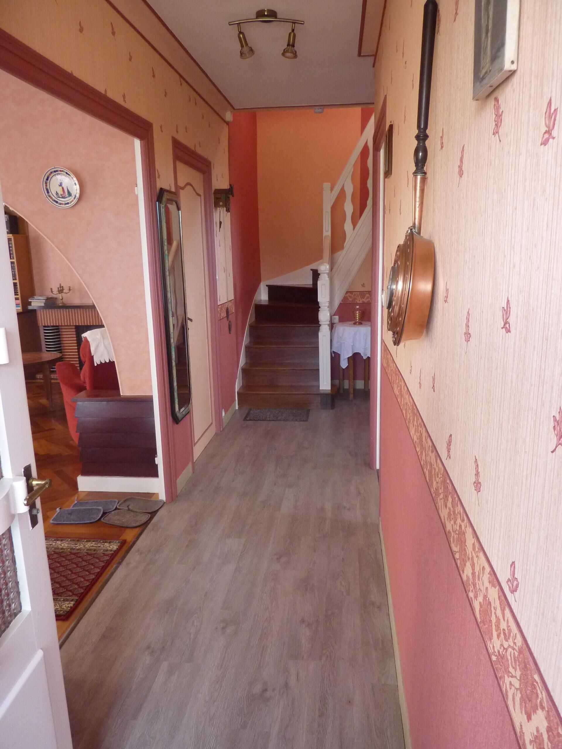Un pasillo con una escalera que sube a un segundo piso. Hay una puerta a la izquierda con una placa decorativa encima.