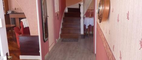 Un pasillo con una escalera que sube a un segundo piso. Hay una puerta a la izquierda con una placa decorativa encima.