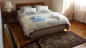 A bedroom with a large bed, a wooden chair, a nightstand, a lamp, and a window with curtains. - Detached house with garden for 2 to 5 people (Plounévez-Lochrist)