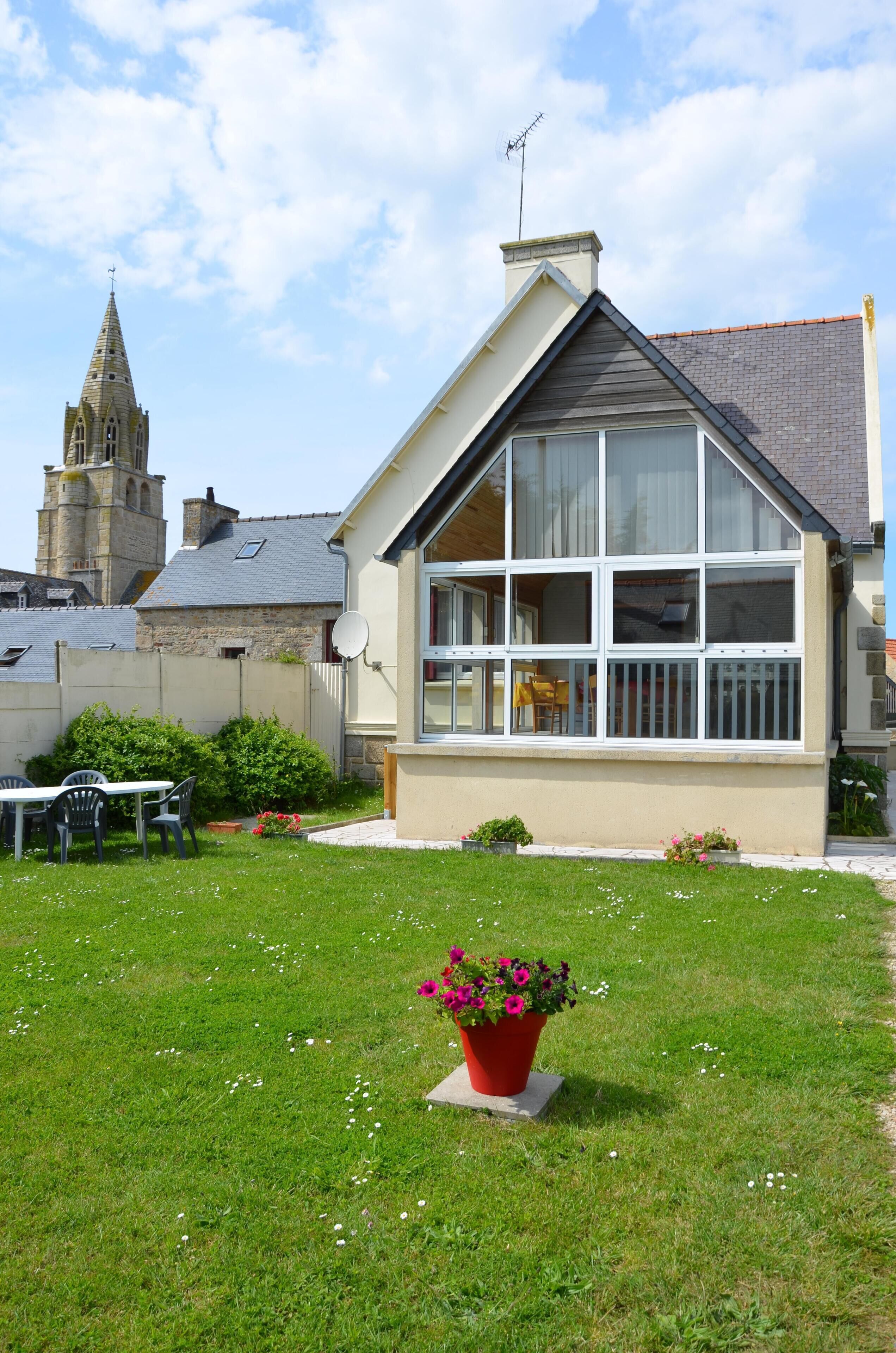 A house with a large window, a satellite dish, and a garden with a red flower pot.