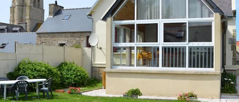 Ein Haus mit großem Fenster, Satellitenschüssel und Garten mit rotem Blumentopf.