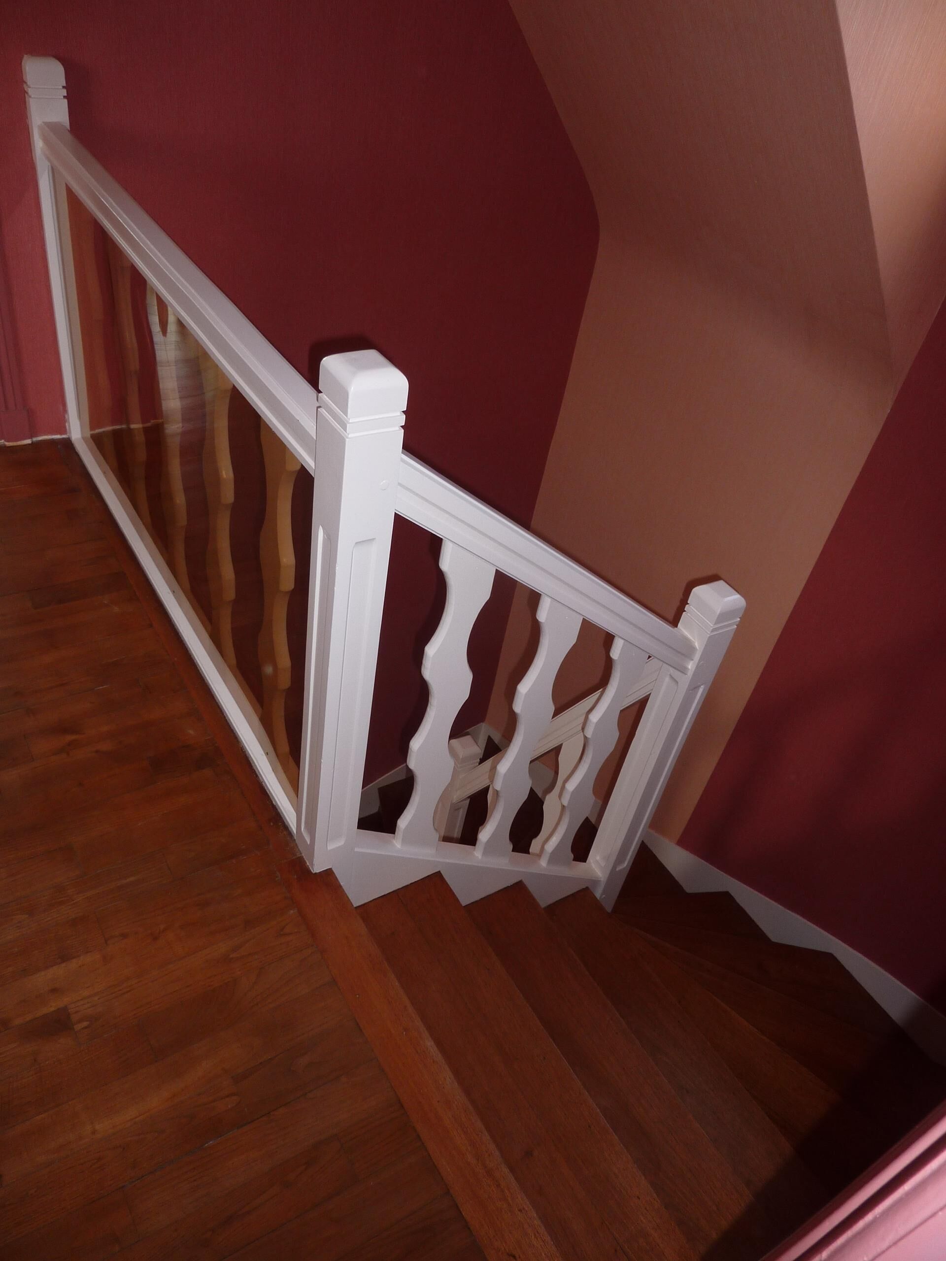 A wooden staircase with white balusters and a red wall.