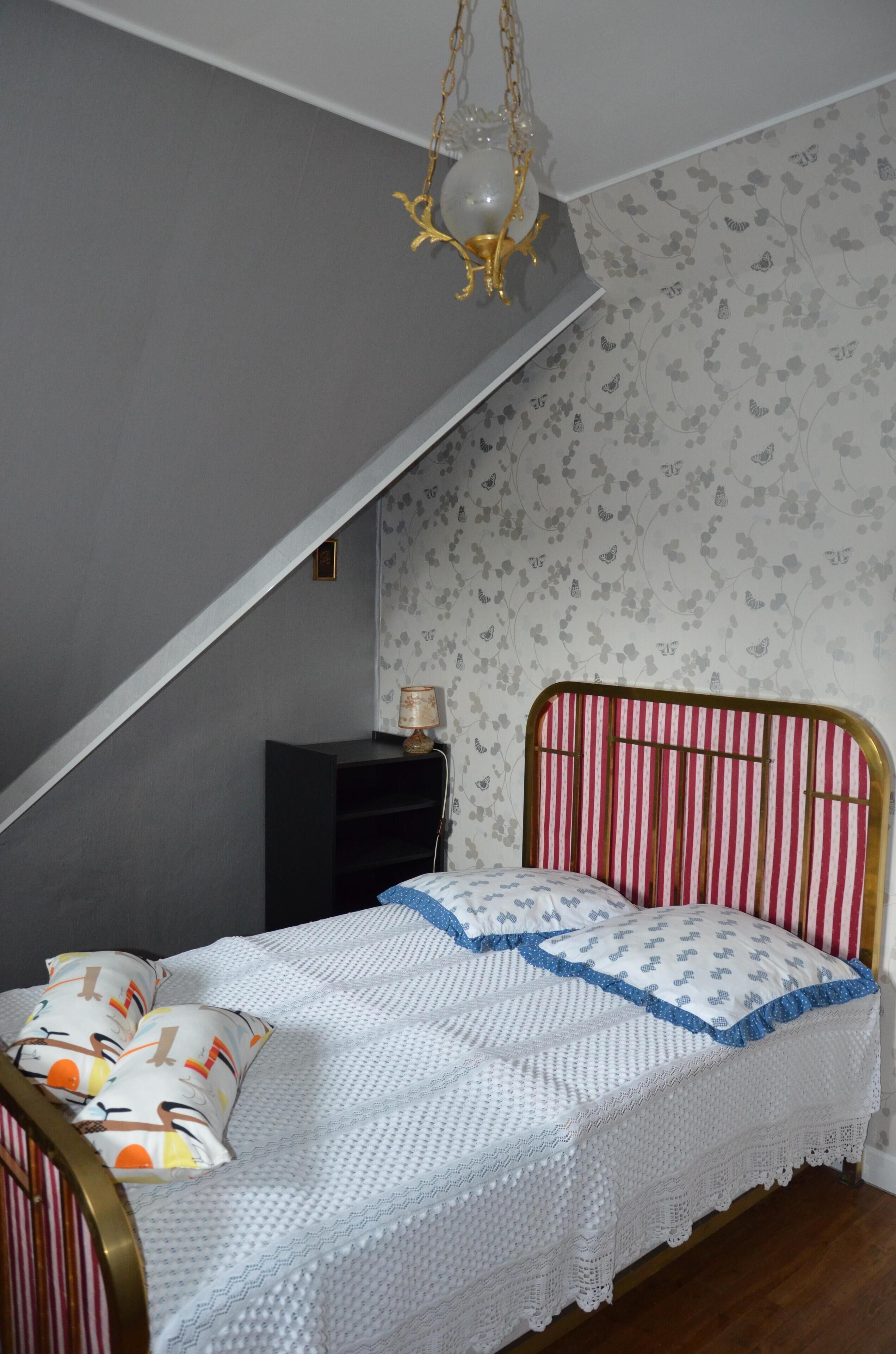 A bedroom with a bed, a nightstand, a lamp, and a hanging light fixture.