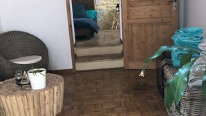 Una habitación acogedora con piso de madera en patrón chevron, una silla de mimbre, una mesita de madera y una cesta de mimbre con toallas.