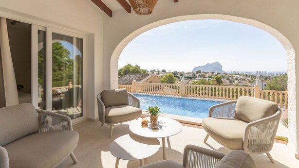Un balcon avec une piscine, des meubles en osier et une vue sur un paysage montagneux.