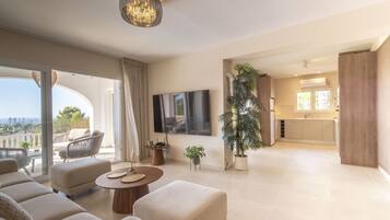 Un amplio salón con televisor grande, asientos cómodos, mesa de comedor y vistas a la ciudad.