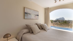 Une chambre avec un grand lit, un tableau et une vue sur une montagne et une ville, visible par la fenêtre.