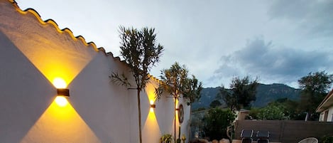 A wooden deck with outdoor furniture, a wall-mounted light fixture, and a rocky landscape.
