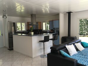 Une cuisine moderne dotée d’un îlot central, de tabourets de bar et d’un canapé en cuir noir agrémenté de coussins à motifs.
