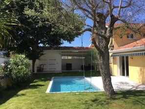 Une piscine entourée d’une pelouse bien entretenue, d’un arbre et d’un bâtiment dont le toit est recouvert de tuiles.