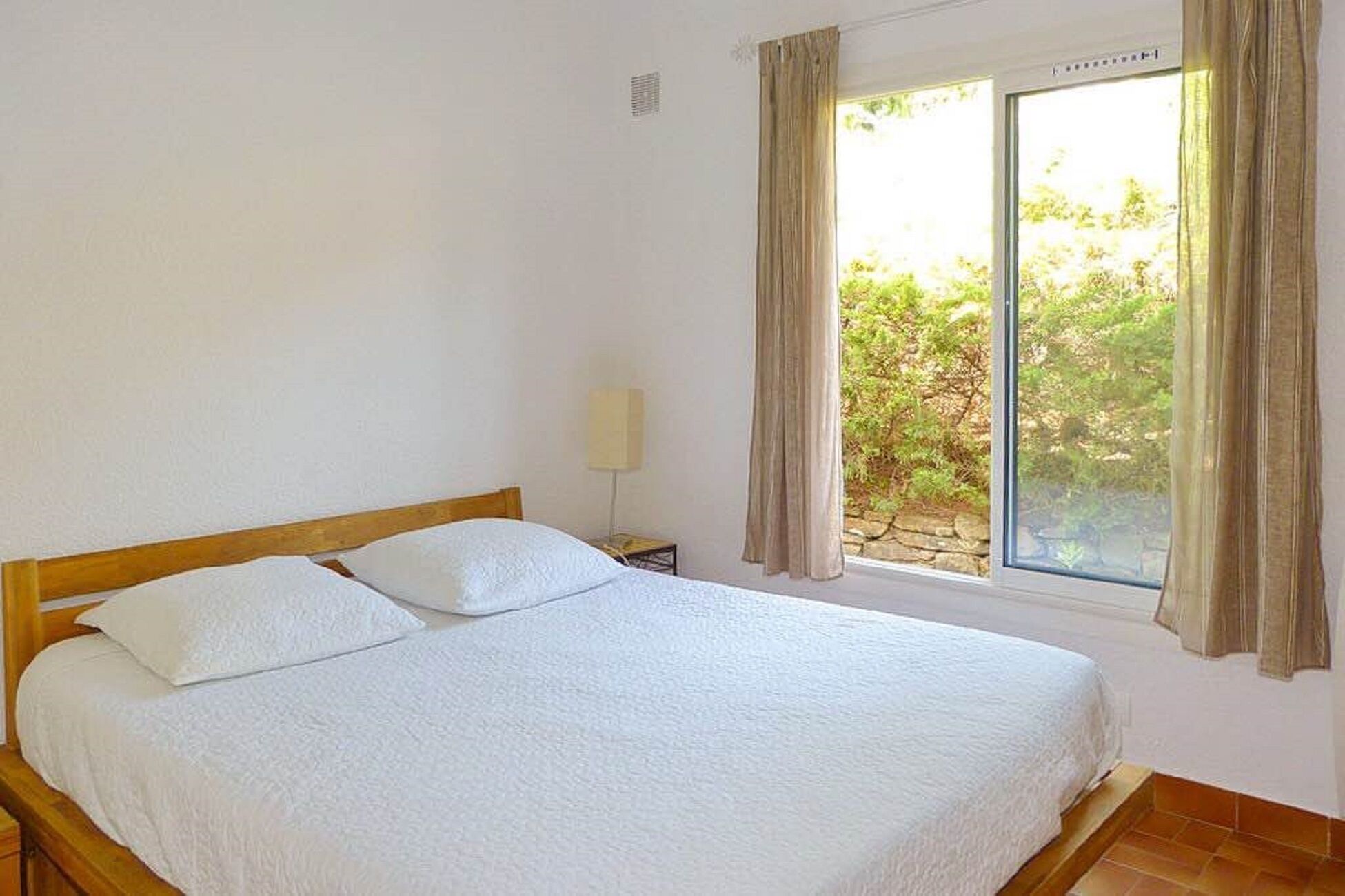 Une chambre à coucher avec un lit en bois, une table de chevet, une lampe et une fenêtre avec des rideaux.