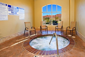 A hot tub area with a view of red rock formations through a window, surrounded by chairs and a warning sign about lifeguards.