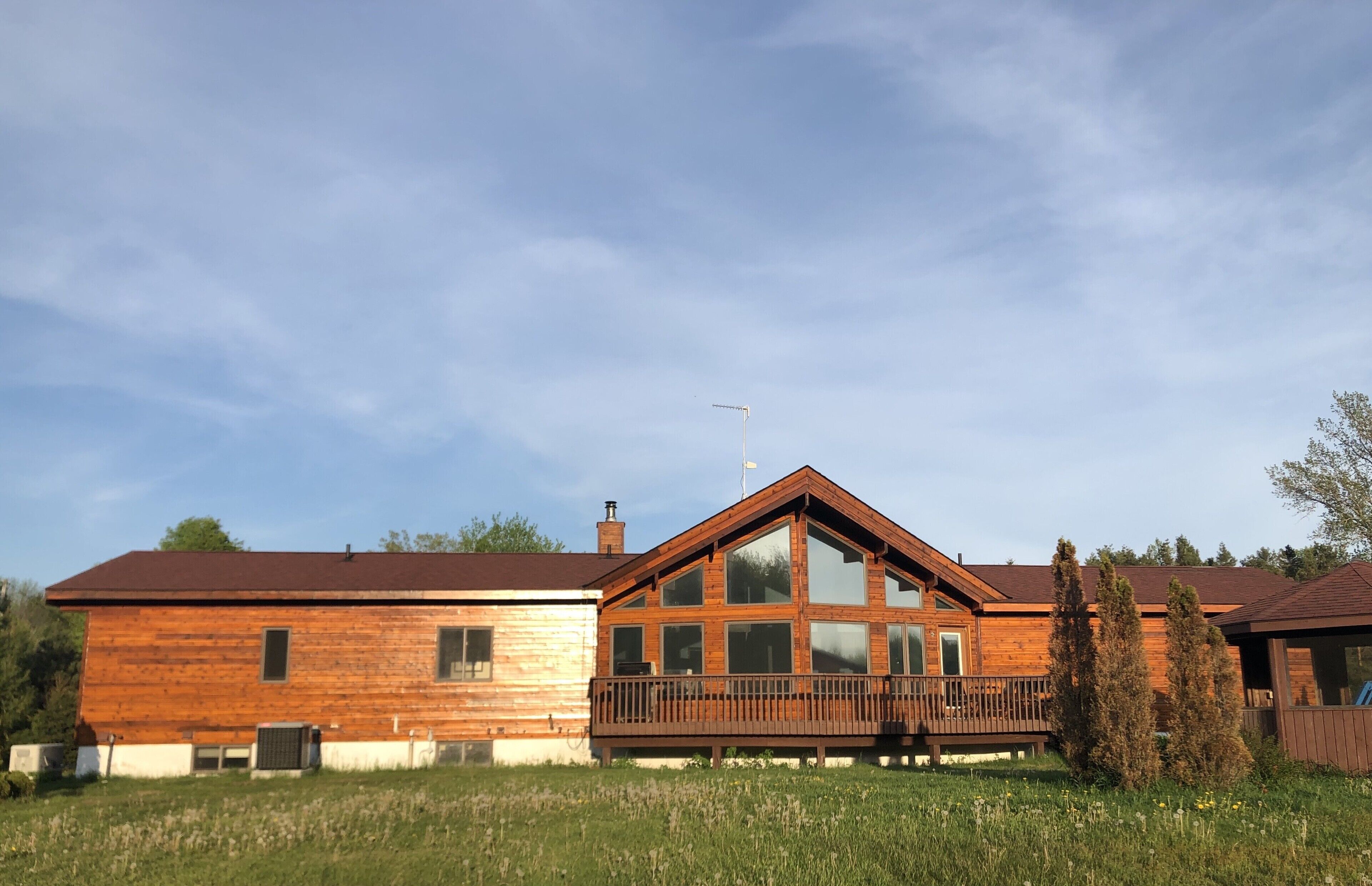 A wooden cabin with a large deck, a chimney, and a satellite dish.