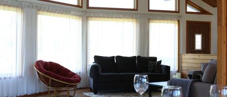 Een gezellige woonkamer met een zwarte bank, een rode fauteuil en een eettafel gedekt voor twee personen, compleet met wijnglazen.