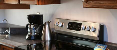 A kitchen with a stainless steel stove, wooden cabinets, and a coffee maker.