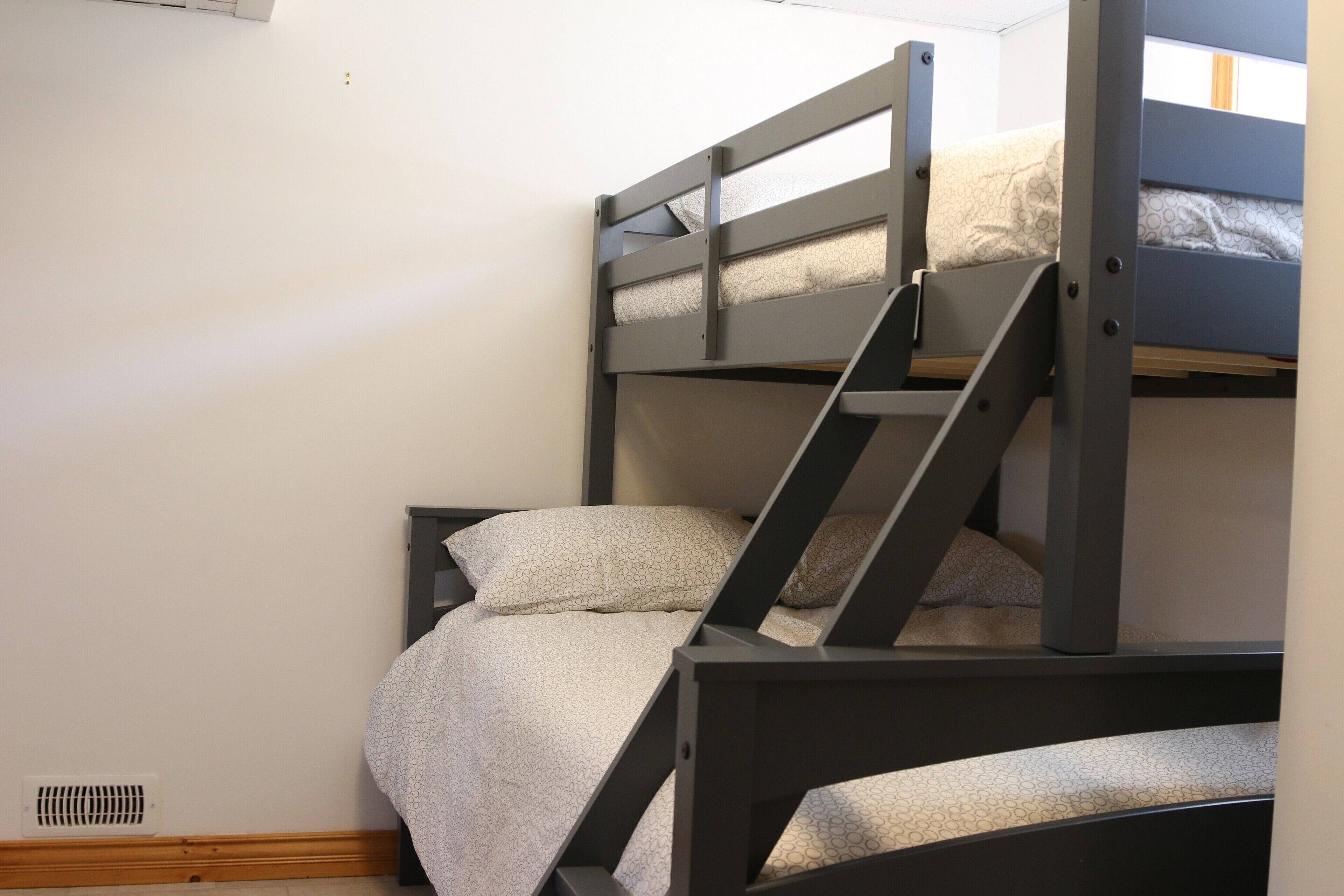 A bunk bed with a ladder, a vent on the wall, and a window with curtains.