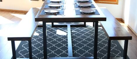 A dining table set with plates, glasses, and cutlery, surrounded by benches on a patterned rug.