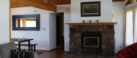 A living room with a stone fireplace, wooden ceiling beams, a sofa, a dining table with glasses, and a red chair.