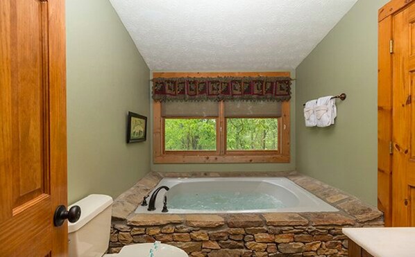 A bathroom with a stone bathtub, a toilet, and a window with a view of trees.