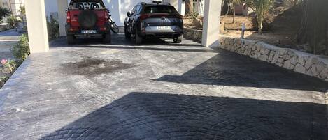 A covered parking area with two SUVs parked under a white structure.