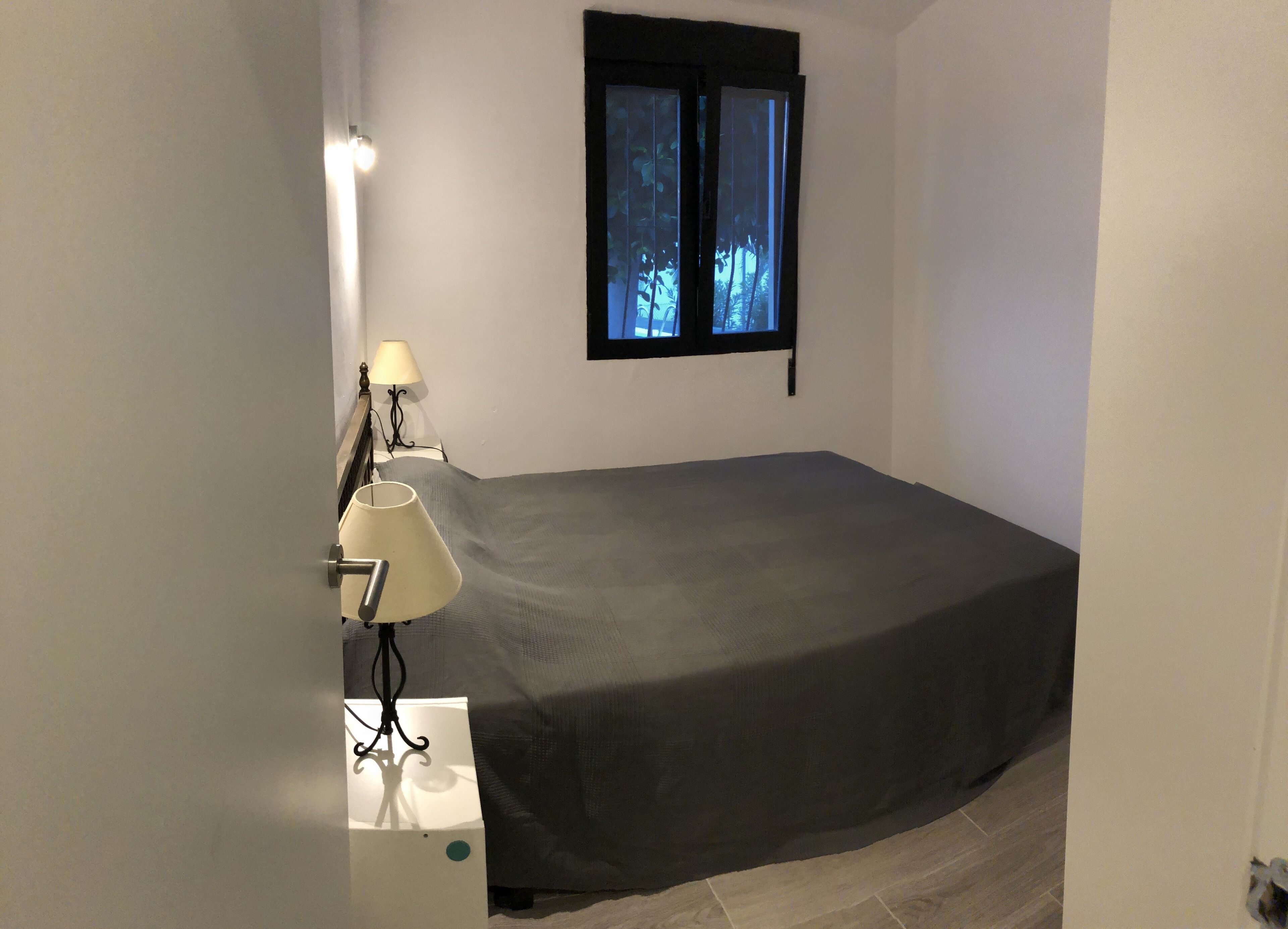 Un dormitorio con cama, dos lámparas de noche, ventana con vistas y televisor en la pared.