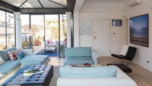 En moderne stue med en hjørnesofa, en sort skammel og en stribet lænestol. Der er en glasdør, der fører til en udendørs patio.