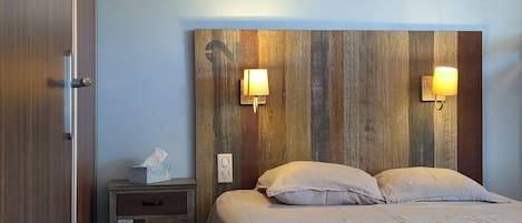 A bedroom with a wooden headboard, two bedside lamps, a bedside table with a tissue box, and a bed with two pillows.