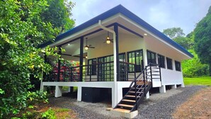 Een modern gebouw met een overdekte veranda, een trap en uitzicht op weelderige begroeiing.