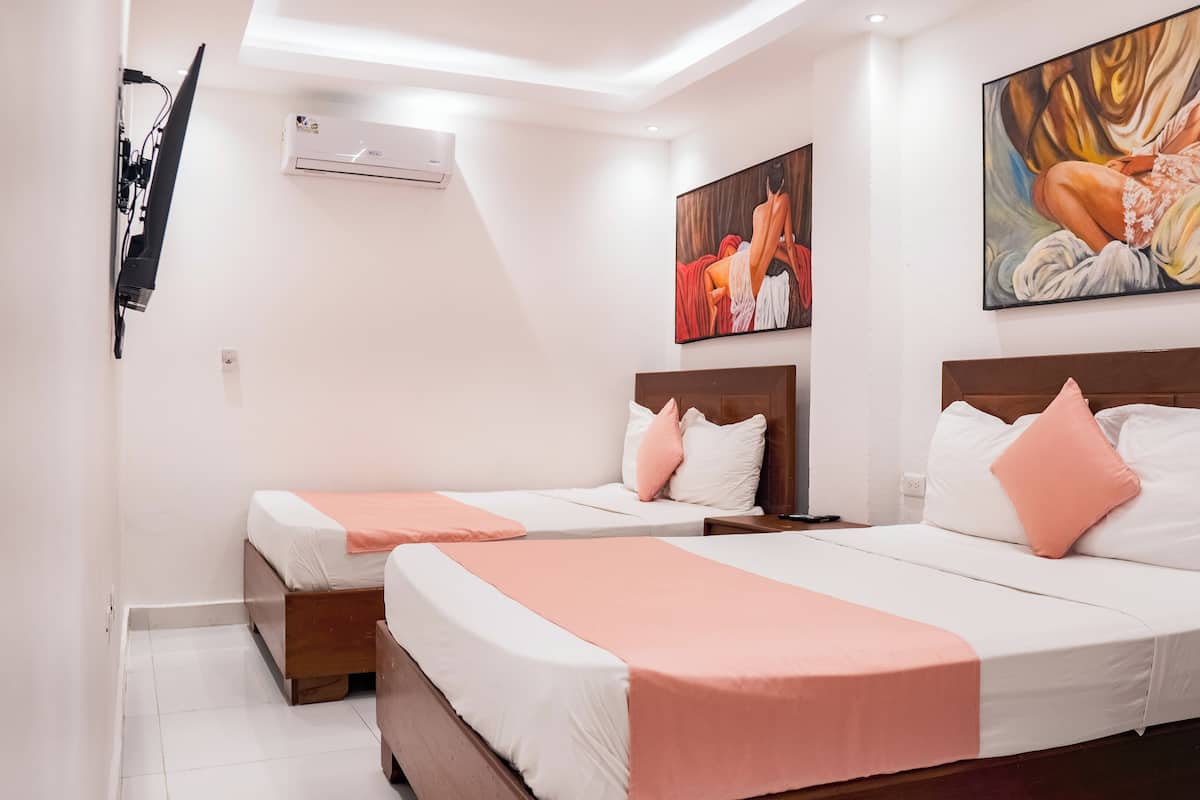 A hotel room with two beds, each with white linens and pink accents, a ceiling fan, an air conditioning unit, and artwork on the walls.