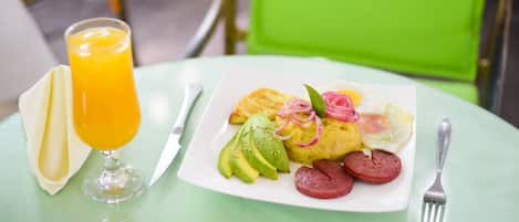 A breakfast plate with eggs, avocado, and sausage, and a glass of orange juice on a green table.