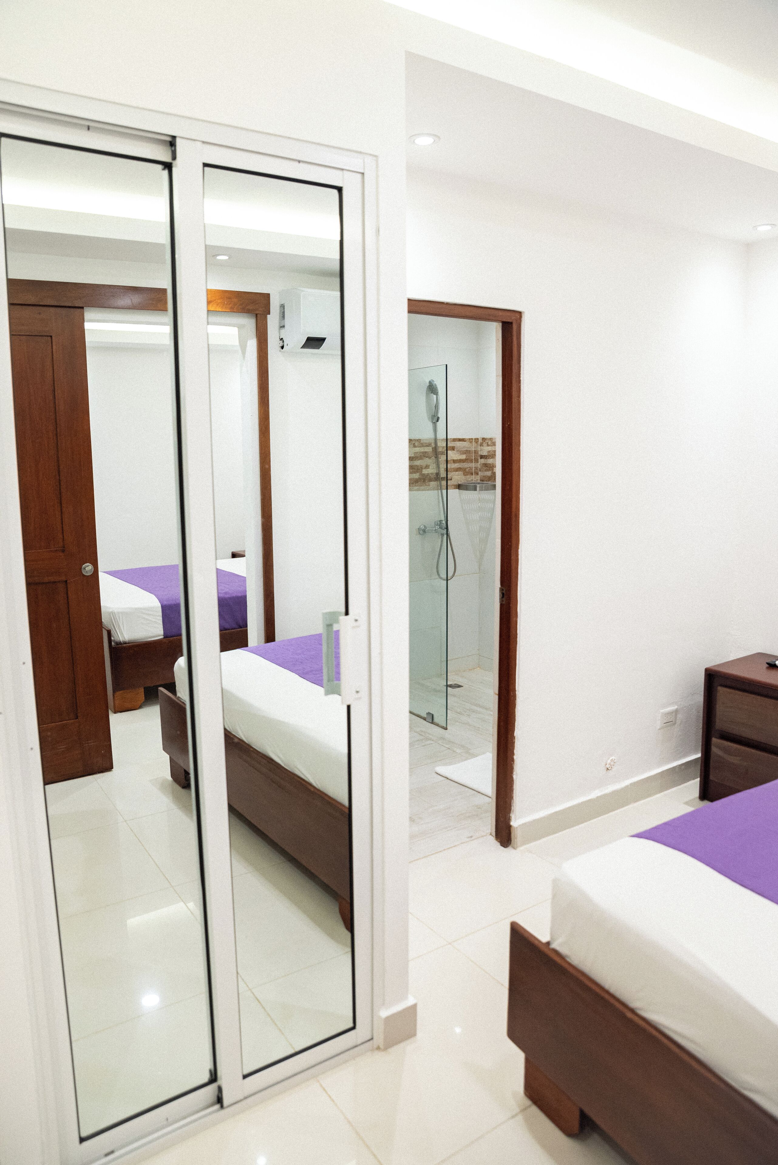 Un dormitorio moderno con un espejo grande, una cama, una mesita de noche y un área de ducha.