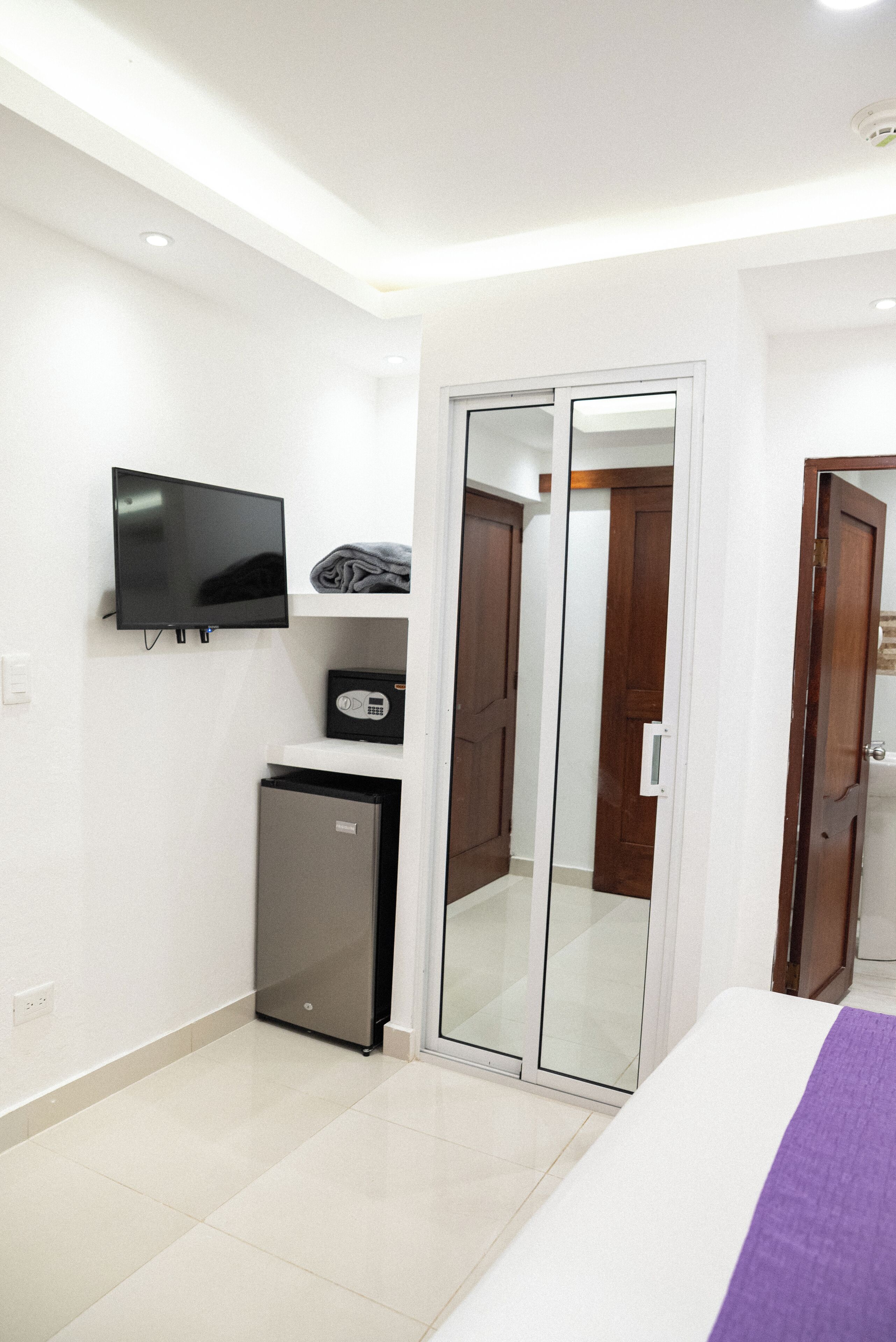 A bedroom with a bed, a television, a mini fridge, and a wardrobe with a mirror.